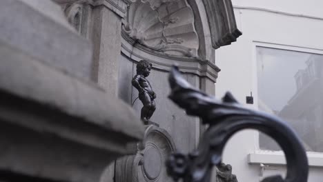 Manneken-Pis-seen-from-behind-the-fence-in-the-city-center-of-Brussels,-Belgium
