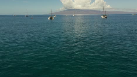 Aerial-Low-Flying-Above-Kahoma-Stream-Off-West-Maui-Towards-Moored-Catamarans-With-View-Of-Lanai-Island-In-The-Background