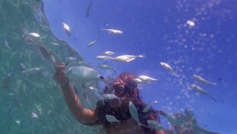 Ungewöhnliche-Unterwasserperspektive-Eines-Kleinen-Mädchens-Aus-Meerwasser,-Das-Fischschwärme-Füttert