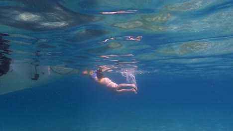 Slow-motion-under-water-surface-scene-of-woman-floating-in-sea-water-beneath-surface-close-to-motorboat-ladder