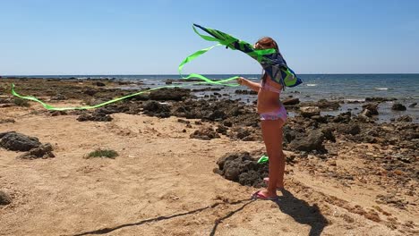 Cute-little-girl-on-summer-holiday-in-swimsuit-on-the-beach-prepares-to-play-with-a-green-toy-kite