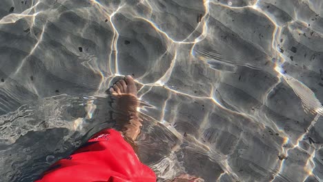 Hochwinkelige-Persönliche-Perspektive-Männlicher-Beine-Und-Füße-Und-Rote-Badebekleidung,-Die-In-Kristallklarem,-Seichtem-Meerwasser-Spazieren-Gehen