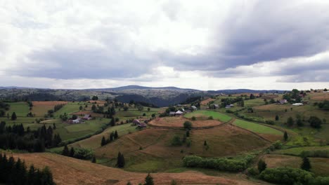 Aerial-picturesque-agricultural-green-hill-land-with-houses-in-countryside