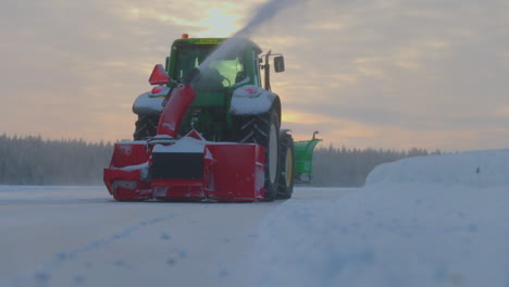 Tractor-snow-blower-clearing-Norbotten-Sweden-ice-track-snowdrift-at-sunrise,-Low-angle,-rear-view