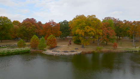 Slow-push-over-a-pond-and-towards-trees-at-peak-color-in-Autumn-at-a-park-in-Kirkwood-in-St