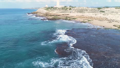Aerial:-The-turqouise-coastline-of-Cadiz,-Spain,-while-waves-are-splashing-against-the-rocks