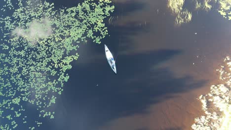 Drone-Filmando-A-Un-Hombre-Pescando-Desde-Una-Canoa-En-Un-Lago-Con-Hojas-Verdes-Y-Hierba