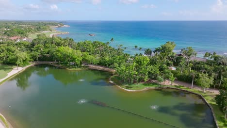Aerial-flight-over-private-natural-lake,-tropical-palm-trees-and-blue-Caribbean-Sea-in-Background-during-sunny-day---Punta-Aguila-in-Dominican-Republic