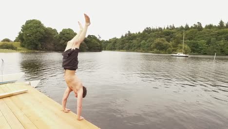 Young-man-performs-handstand-dive-off-the-jetty-into-river