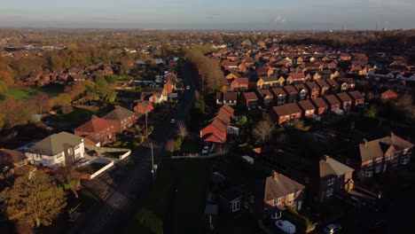 English-suburban-village-neighbourhood-homes-glowing-in-Autumn-golden-hour-sunlight-aerial-panning-view