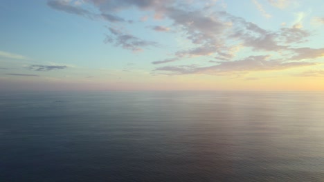 High-altitude-drone-pan-over-tranquil-ocean-waters-during-a-majestic-sunset