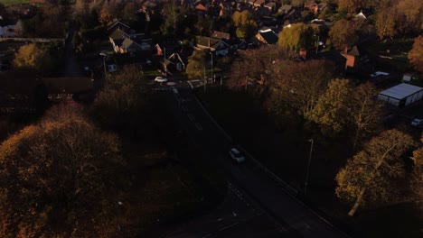 English-village-road-surrounded-by-autumn-trees-aerial-view-tilting-to-countryside-neighbourhood-at-golden-hour