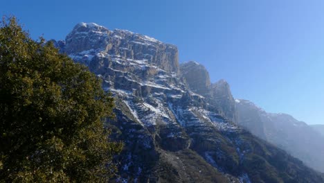 Cimas-De-Montañas-Rocosas-Y-Nevadas-Aparecen-Detrás-De-Un-árbol-En-Zagori,-Grecia