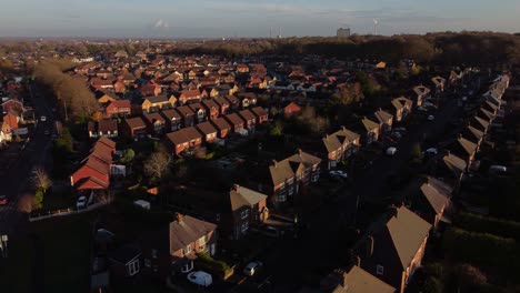British-suburban-village-neighbourhood-homes-glowing-in-Autumn-golden-hour-sunlight-aerial-panning-view