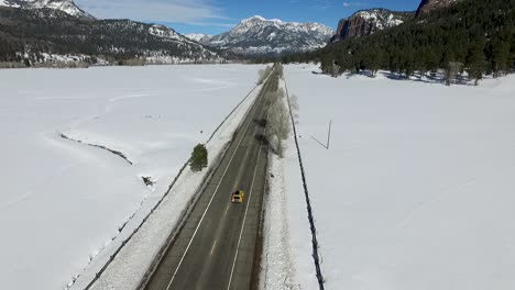 Aerial-drone-hovering-next-to-a-highway-in-a-snowy-winter-mountain-with-cars-driving-through