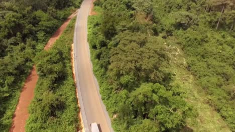 Aerial-drone-view-of-a-truck-driving-on-a-road,-through-the-forest,-on-a-sunny-day,-in-Nanga-Eboko,-Haute-Sanaga,-Southern-Cameroon