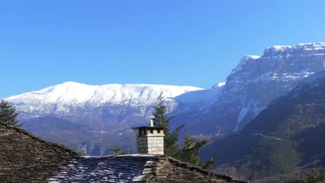 Traditional-stone-roof-with-snowy-mountains-in-the-background-in-Zagori,-Greece