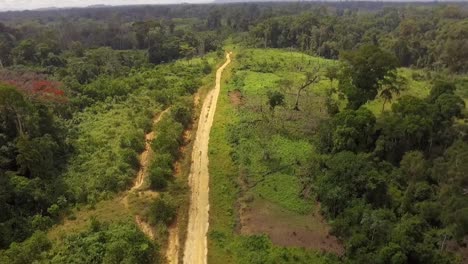 Aerial-drone-view-flying-backwards-over-a-small-sand-road,-in-the-Jungle,-on-a-sunny-day,-in-Nanga-Eboko-forest,-Haute-Sanaga,-Southern-Cameroon