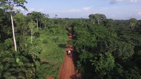 Video-from-high,-the-drone-flies-forward-as-it-follows-a-white-off-terrain-vehicle-through-the-dirt-path-that-flows-through-the-forest