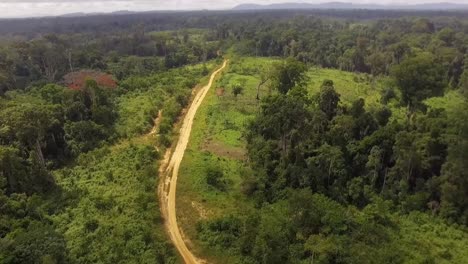 Aerial-drone-view-towards-a-small-sand-road,-in-the-Jungle,-on-a-sunny-day,-in-Nanga-Eboko-forest,-Haute-Sanaga,-Southern-Cameroon