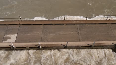 High-angle-view:-Flooding-river-water-reaches-deck-of-one-lane-bridge