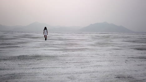 Dramatic-aerial-of-woman-walking-in-dress-in-Utah-desert-salt-flat
