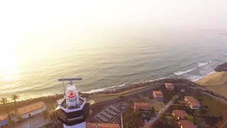 Drone-footage-flying-towards-a-light-house-with-a-look-down-movement-with-early-morning-beach-in-the-back-ground