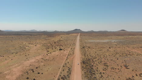 Antenne-Der-Namibischen-Landschaft-Mit-Dem-Auto,-Das-In-Der-Ferne-Auf-Einer-Staubigen-Straße-Unterwegs-Ist