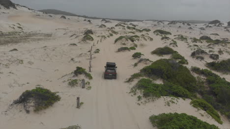 Vehicle-driving-around-sandy-beach-with-grassy-dunes