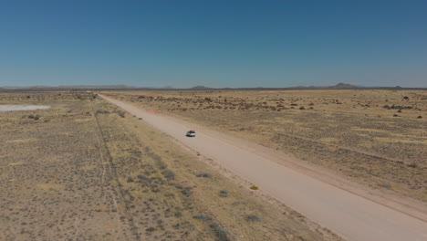 Aerial-diagonal-follow-shot-from-rear-of-vehicle-travelling-along-dusty-empty-long-highway