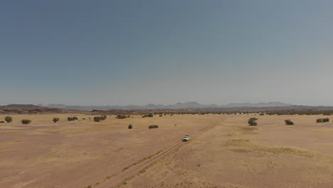 Left-aerial-panning-shot-in-front-of-vehicle-driving-alone-in-desert-at-distance