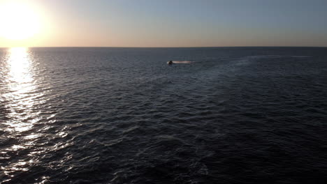 A-Woman-on-a-Jet-Ski-Speeds-Past-the-Camera-on-an-Open-Ocean-During-Sunset