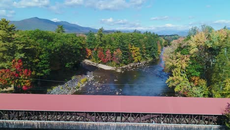 Sunny-rising-shot-of-covered-bridge-in-the-fall-with-people-to-reveal-mountains