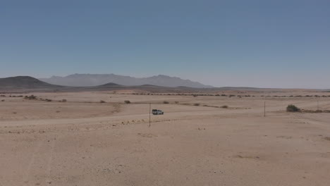 Side-aerial-follow-shot-of-vehicle-travelling-on-empty-desert-road
