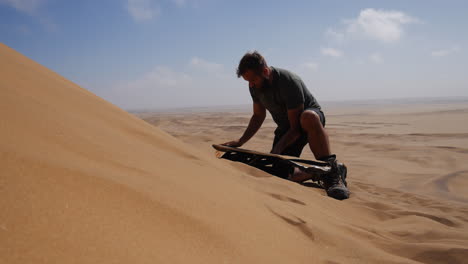 Guy-on-sandy-dune-waxing-sand-board
