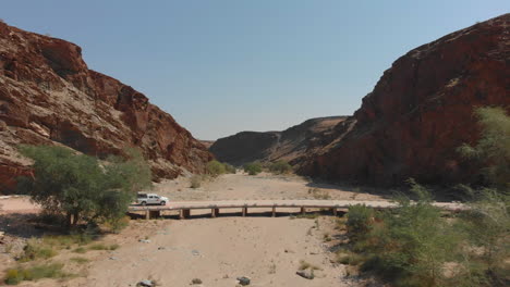 Vehicle-passing-over-bridge-between-mountain-range-dry-river-bed