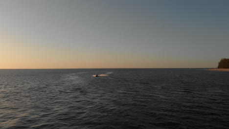 A-Woman-Riding-on-a-Jet-Ski-Speeds-Past-the-Camera-on-an-Empty-Ocean-During-a-Beautiful-Sunset