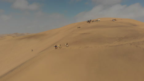 Aerial-shot-of-people-walking-up-sand-dune-with-sand-boards