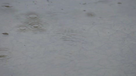 Regenwasserpfütze-Auf-Einem-Gerissenen-Zement-Im-Regen-Mit-Einigen-Blasen