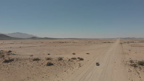 Right-panning-shot-over-vehicle-driving-alone-on-desert-road