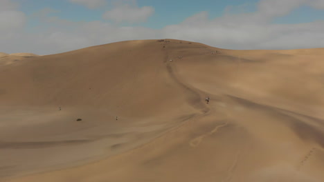 People-walking-up-sand-dune-with-sand-boards