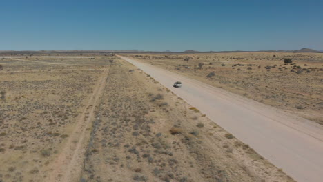 Aerial-rotating-follow-shot-of-fast-moving-vehicle-on-empty-dusty-highway-in-desert