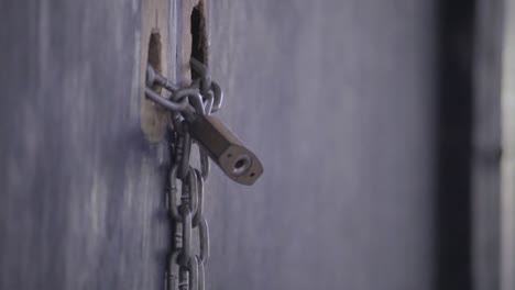 Close-up-of-lock-and-chain,-locking-a-old-ugly-wooden-door