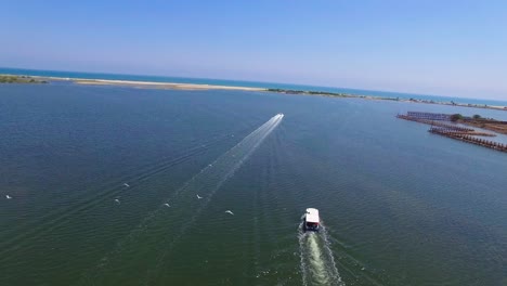 Drone-shot-flying-across-mouth-of-backwater-channel-with-two-boats-,-one-passenger-boat-an-one-speed-boat-crossing-the-frame