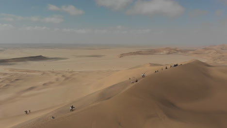Aerial-rotation-around-sand-boarders-heading-up-large-dune