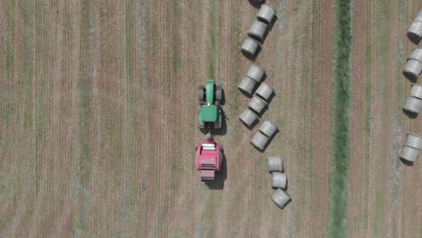 Aerial-top-down-shot-of-tractor-driving-past-round-bales-of-hay