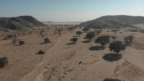 Ferne-Luftaufnahme-Nach-Dem-Fahrzeug,-Das-In-Der-Afrikanischen-Wüste-Des-Trockenen-Flussbettes-Fährt