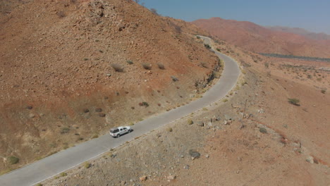 Aerial-following-car-travelling-up-steep-road-in-desert-mountains