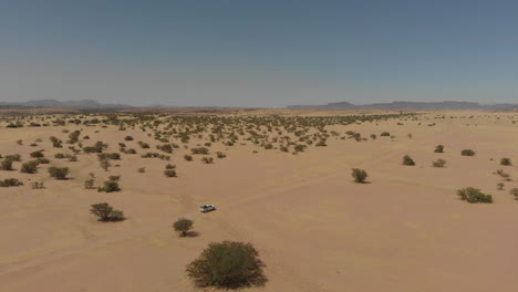Distant-aerial-follow-shot-of-vehicle-driving-alone-through-desert