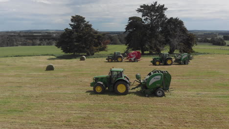 Aerial-side-following-shot-of-3-tractors-driving-on-paddock-making-hay-bales